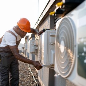African man in uniform checking air conditioner on plant